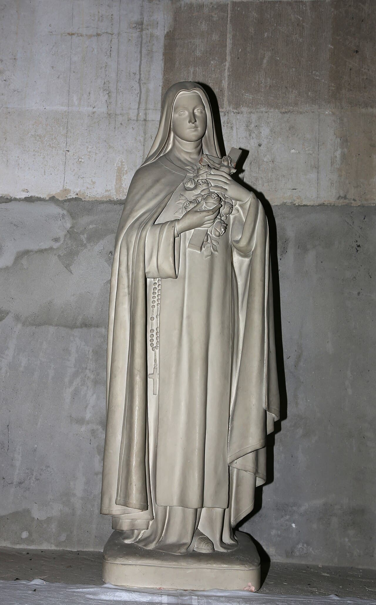 Estátua de Santa Teresinha de Lisieux segurando rosas e um crucifixo